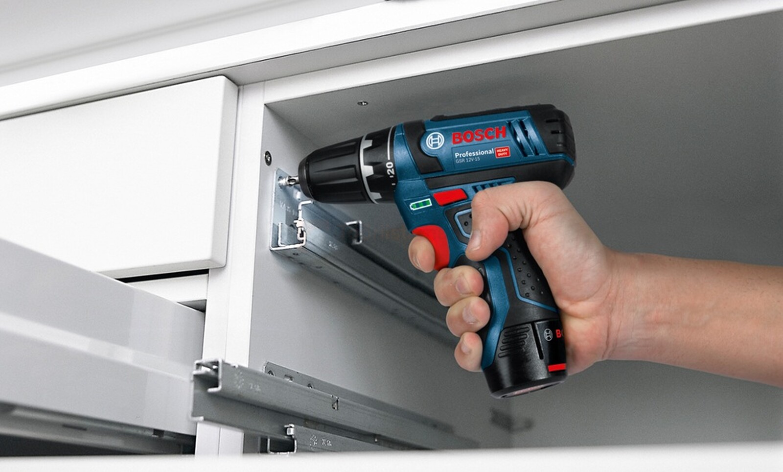 Pildil on näha, kuidas inimene kasutab Bosch GSR 12V-15 akutrelli kapi sisse kruvide keeramiseks.